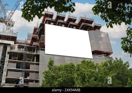 Leeres weißes Banner für Werbung, das auf dem Gerüst eines modernen Gebäudes im Bau hängt. Weißes Informationsbanner an der Wand Stockfoto