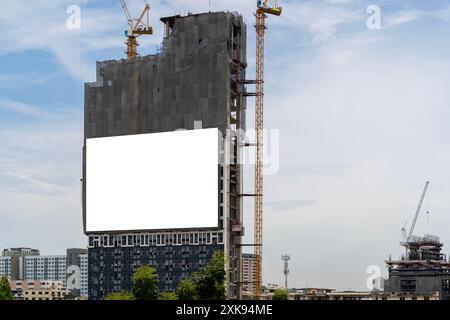 Leeres weißes Banner für Werbung, das auf dem Gerüst eines modernen Gebäudes im Bau hängt. Leere weiße Werbebanner an der Wand von m Stockfoto