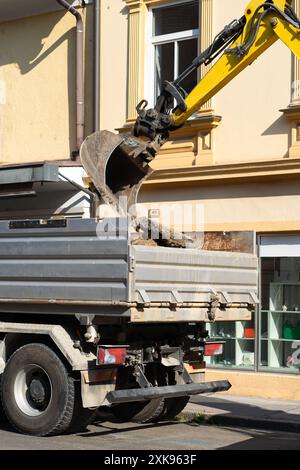 Der Baggerlöffel stapelt alten Asphalt in das LKW-Bett. Stockfoto