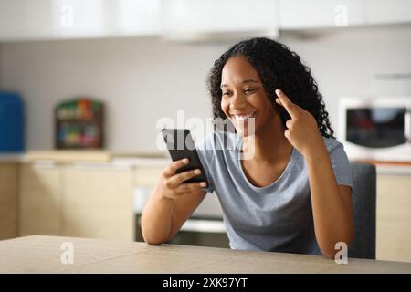 Glückliche schwarze Frau, die die Finger drückt und in der Küche zu Hause telefoniert Stockfoto