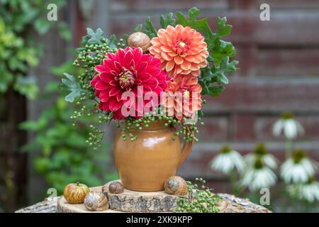 Bouquet aus roten und orangen Dahlien, Holunderbeeren und Eichenblättern in einer rustikalen Vase Stockfoto