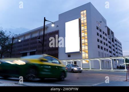 Leere Reklametafeln und Hochhaus-Geschäftsgebäude in der Nacht. Eine helle leere Plakattafel hebt sich am Abend von der umliegenden Innenstadt ab Stockfoto