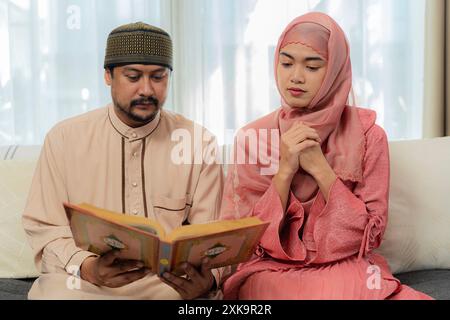 Asiatische muslimische Familie liest zu Hause den koran zusammen. Asiatisch-muslimischer Mann, der Ehefrau unterrichtet, Koran oder Koran im Wohnzimmer zu lesen Stockfoto