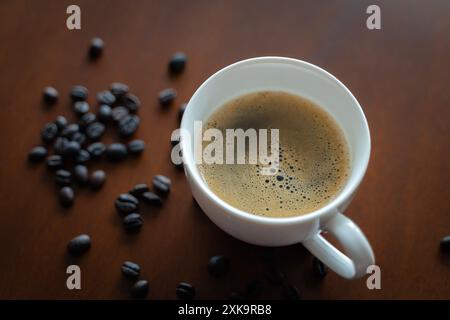 Tasse Espresso mit Kaffeebohnen auf Holztisch. Hintergrund der Struktur des gemahlenen Kaffees. Kaffeebohnen sind auf dem Tisch verstreut. Stockfoto