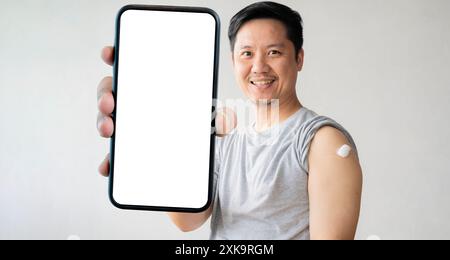 Ein Mann lächelt, nachdem er einen Impfstoff bekommen hat. Ein Mann hält ihm den Hemdschuh herunter und zeigt ihm den Arm mit Verband, nachdem er Akzination erhalten hat, und hält einen großen sm Stockfoto