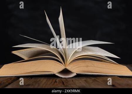 Öffne das Bibelbuch auf einem dunklen Tisch. Unauffälliges Bild des Neuen Testaments in hellem Licht zwischen Dunkelheit und Schatten, Bild eines offenen antiken Buches auf Holztisch Stockfoto