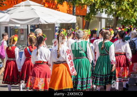 Bulgarische Frauen in traditioneller Volkskleidung gehen in die Stadt, bunte Röcke und Blusen mit Blumen im Haar Stockfoto