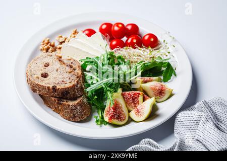 Frühstücksteller mit Brot, Tomaten, Brie-Käse, Rucola, Nüssen und Feigen auf weißem Hintergrund. Stockfoto