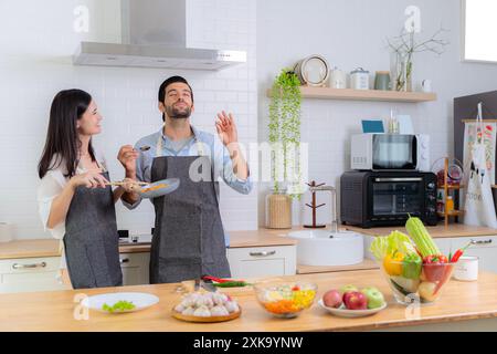 Der Typ war sehr glücklich, die Kochkünste seiner Freundin zu probieren. Junge verliebte Paare, die Spaß haben, während sie ein gemeinsames Frühstück auf einem schönen Mo zubereiten Stockfoto