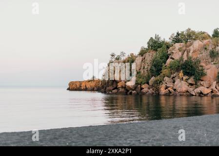 Felsige Klippe am ruhigen Wasser in der Dämmerung. Stockfoto