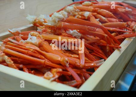 Gekochte Krabbenbeine in einer Holzkiste auf einem Holztisch. Stockfoto