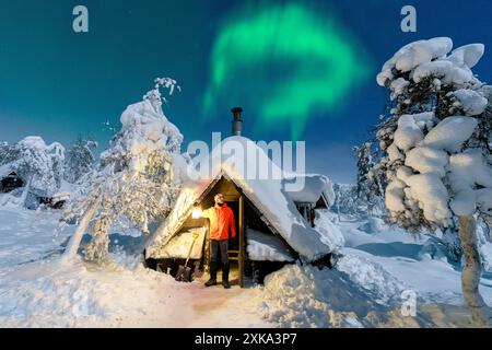 Wanderer mit Laterne, die Nordlichter von einer verschneiten Berghütte aus bewundern Stockfoto