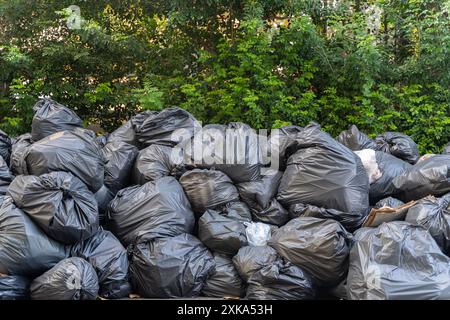 Schwarze Mülltüte stapeln sich. Zerknitterte Kunststoffbeutel. Viele biologisch abbaubare Beutel stapelten sich an einer Wand aus Blättern. Stockfoto