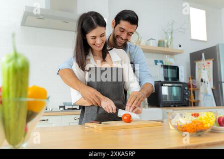 Junge Paare, die Spaß haben, während sie gemeinsam das Frühstück an einem schönen Morgen vorbereiten, zusammen kochen, Küchenbeziehung, Tomaten zusammen schneiden. L Stockfoto