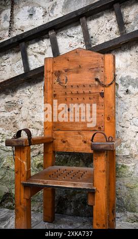 Der antike hölzerne Folterstuhl mit Metallfesseln steht vor einer Steinmauer und weckt ein erschütterndes Gefühl der Furcht und die Brutalität des Papas Stockfoto