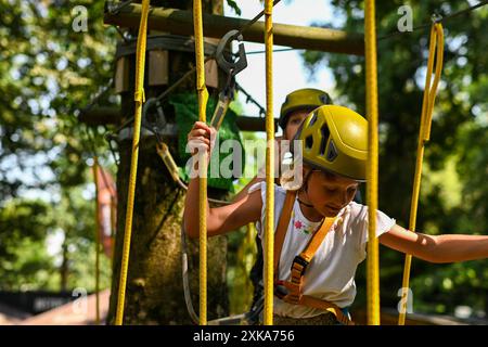 Zwei Kinder tragen Sicherheitsgurte und Helme, die einen Seilkurs in einem Park steuern. Stockfoto