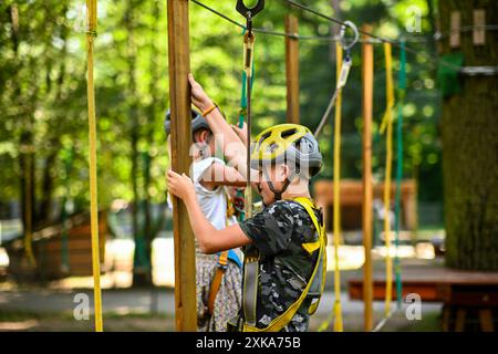 Zwei Kinder tragen Sicherheitsgurte und Helme, die einen Seilkurs in einem Park steuern. Stockfoto