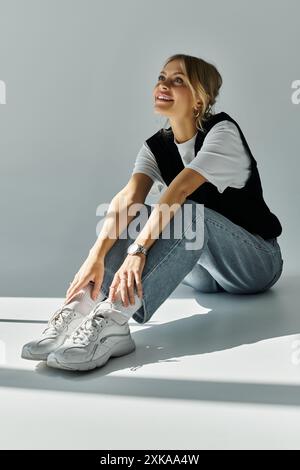 Eine junge blonde Frau sitzt auf dem Boden, hält ein Paar Turnschuhe und strahlt ein Gefühl friedlicher Besinnung aus. Stockfoto