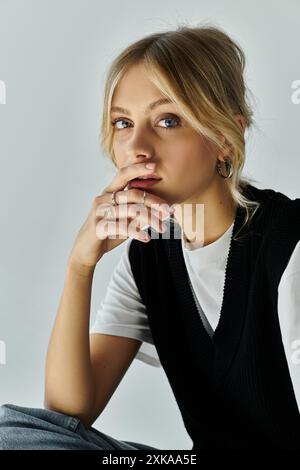 Eine junge Frau mit blonden Haaren sitzt tief in Gedanken auf dem Boden, mit der Hand auf ihrem Kinn. Stockfoto