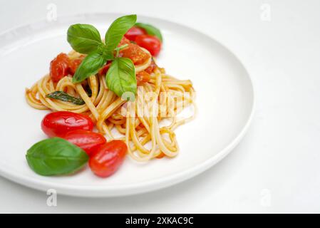 Nudelgericht mit Tomaten und Basilikumblättern. Linguine-Nudeln mit Kirschtomaten und Knoblauchsauce auf einem weißen Teller mit Kopierraum Stockfoto