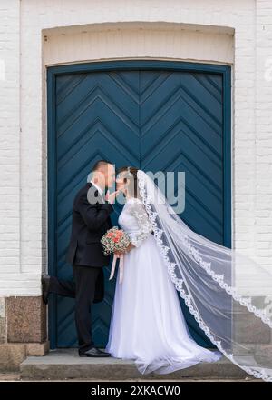 Liebe, Hochzeit und verheiratetes Paar küssen sich vor dem Hintergrund blauer Türen zu Ehren ihrer romantischen Ehe. Traditionell, die Braut und der Bräutigam kis Stockfoto