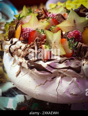 Eine Nahaufnahme eines pavlova-Desserts mit frischen Früchten, einschließlich Erdbeeren, Himbeeren, Sternfrüchten und Schokoladenspänen. Stockfoto