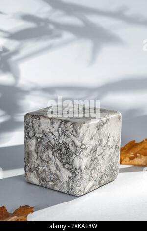 Marmorsteinwürfel Standfuß mit Kopierraum für Produkte und Herbsthintergrund mit Herbstbaumblättern. Weißes Sonnenlicht an der Wand Stockfoto