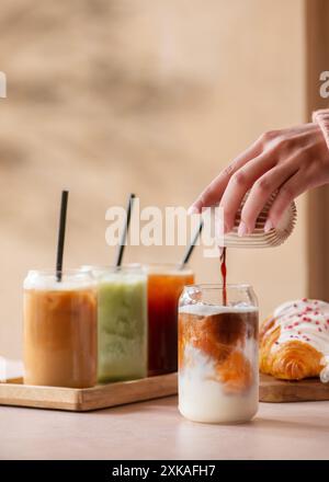Frau, die Kaffee in ein Eisgetränk gießt. Auswahl an Eiskaffee und Matcha-Getränken auf einem Coffee Shop-Tisch. Minimalistisches Konzept. Stockfoto