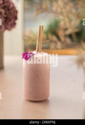 Veganer Smoothie mit Erdbeeren, dekoriert mit Kokosnuss und essbarer Blume auf einem Coffee Shop Tisch. Stockfoto