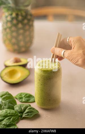 Frau, die ein Glas veganen Avocado- und Spinat-Smoothie auf einem Coffee-Shop-Tisch hält. Stockfoto