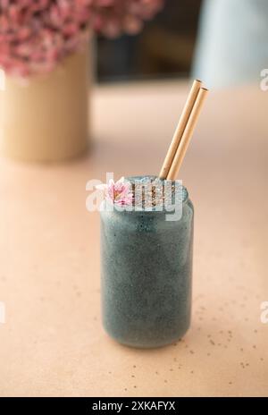 Frau mit einem Glas veganen Beeren-Smoothie, dekoriert mit essbarer Blume. Stockfoto