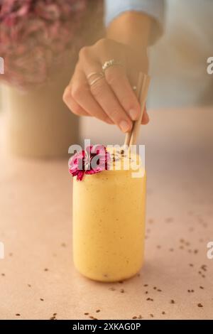 Frauenhand legt einen Strohhalm in ein Glas veganen Mango-Smoothie auf einen Coffee-Shop-Tisch. Stockfoto