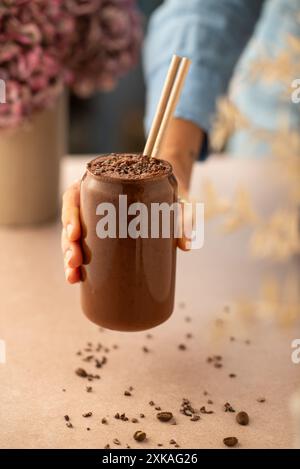 Frau hält ein Glas veganer Schokolade und Kaffee-Smoothie in einem Café. Brauner Smoothie. Stockfoto