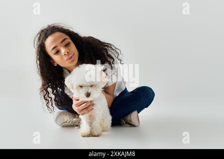 Eine Frau hält friedlich ihren kleinen weißen Bichon Frise Hund in liebevoller Umarmung. Stockfoto