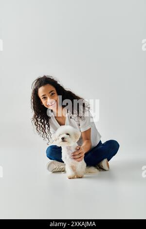 Eine junge Frau kniet anmutig nieder und hält ihren weißen Bichon Frise Hund. Stockfoto