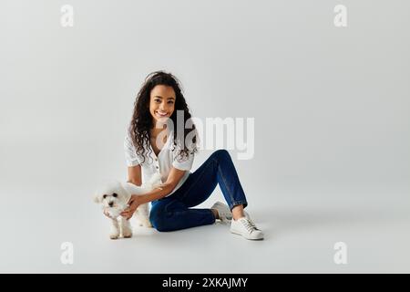 Eine junge Frau sitzt auf dem Boden und hält sanft ihren kleinen Bichon Frise Hund. Stockfoto