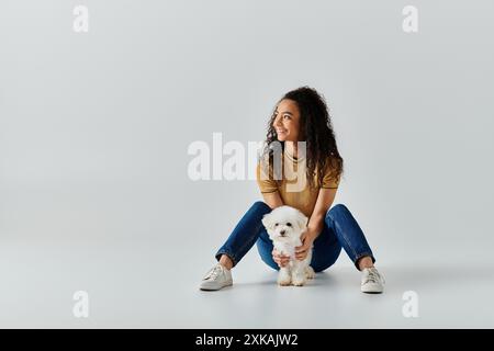 Eine Frau sitzt friedlich auf dem Boden neben ihrem weißen Bichon-Friseurhund. Stockfoto