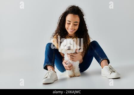 Eine junge Frau sitzt ruhig auf dem Boden und kuschelt einen flauschigen weißen Bichon Frise. Stockfoto