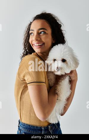 Eine junge Frau hält sanft ein weißes Biconfrise in den Armen. Stockfoto