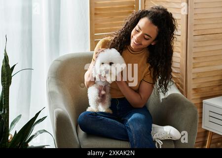 Eine junge Frau sitzt auf einem Stuhl und wiegt einen kleinen weißen Hund in ihren Armen. Stockfoto