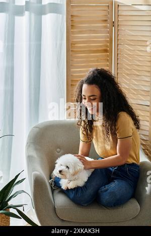 Eine junge Frau, die auf einem Stuhl sitzt und ihren Bichon-Friseurhund hält. Stockfoto