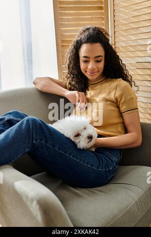 Eine Frau entspannt sich auf der Couch, während sie ihren kleinen weißen Hund hält. Stockfoto