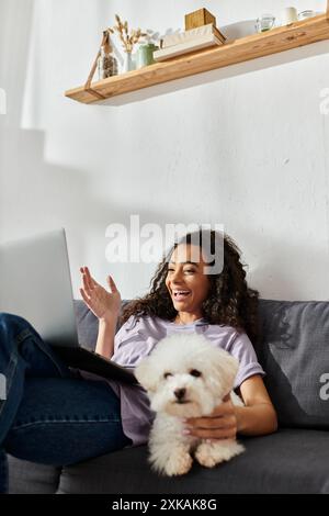 Eine Frau entspannt sich auf einer Couch und wiegt einen weißen Hund in ihren Armen. Stockfoto