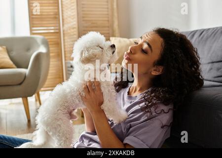 Eine junge Frau entspannt sich auf einer Couch und hält sanft ihren weißen Bichon-Friseehund. Stockfoto