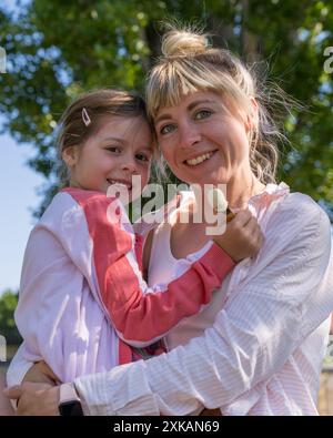 Porträt von Mutter und Tochter. Eine junge Mutter umarmt ihre kleine Tochter zärtlich. Glückliches, lächelndes Mädchen, das Eis in den Händen hält. Beziehungen i Stockfoto