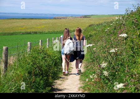 Rückansicht von zwei jungen Mädchen im Teenageralter, die im Sommer auf einem von Wildblumen gesäumten Pfad zum Meer spazieren gehen Pembrokeshire Wales UK KATHY DEWITT Stockfoto