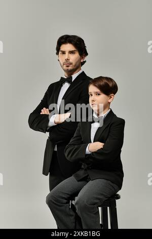 Vater und Sohn stehen zusammen in passenden schwarzen Anzügen, Arme überkreuzt. Stockfoto