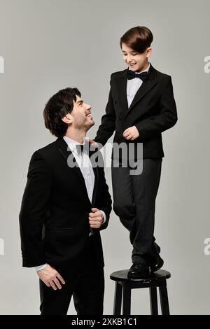 Ein Vater und ein Sohn, beide in Anzügen und Schleifen gekleidet, teilen einen verspielten Moment zusammen. Stockfoto