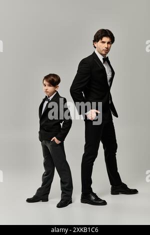 Ein Vater und ein Sohn stehen nebeneinander in passenden schwarzen Anzügen und zeigen eine starke Verbundenheit. Stockfoto