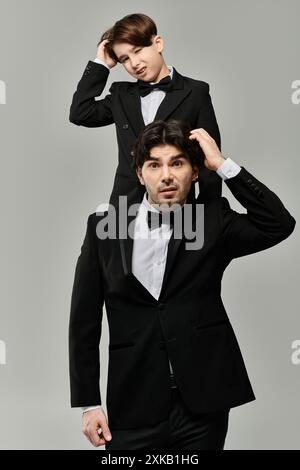Ein Vater und ein Sohn in passenden Smoking-Anzügen stehen vor einem grauen Hintergrund. Stockfoto